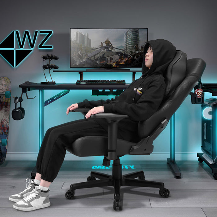 Black Warzone Gaming Chair in a realistic blue-backlit gaming room with a man sitting reclined on the chair.
