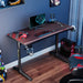 Black GIP 47" Gaming Desk in a realistic setting of a gamer's typical room with peripherals on the desk.
