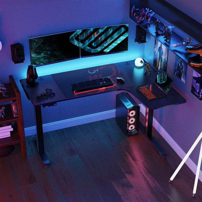 Bird's eye: L-Shaped Electric Standing Desk Left-sided in a simple realistic gamer's room setting with a few gaming peripherals on top.